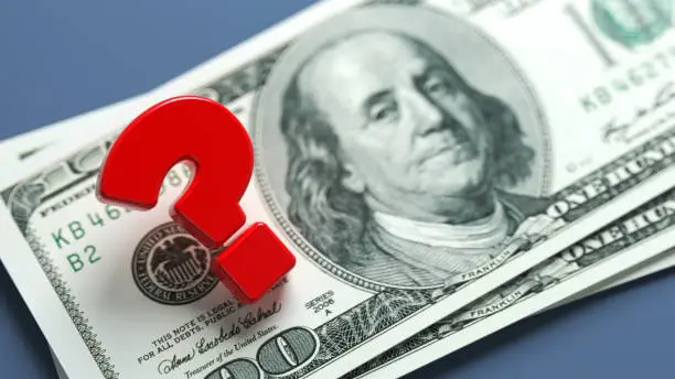 Red-colored question mark symbol and American hundred dollar bill. On grayish blue-colored background. Horizontal composition with copy space. Focused image.