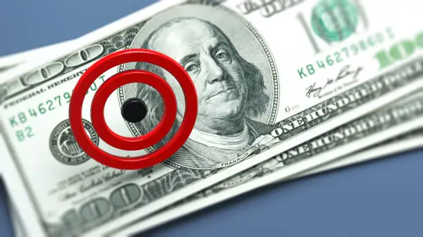 Red-colored target icon and American hundred dollar bill. On grayish blue-colored background. Horizontal composition with copy space. Focused image.