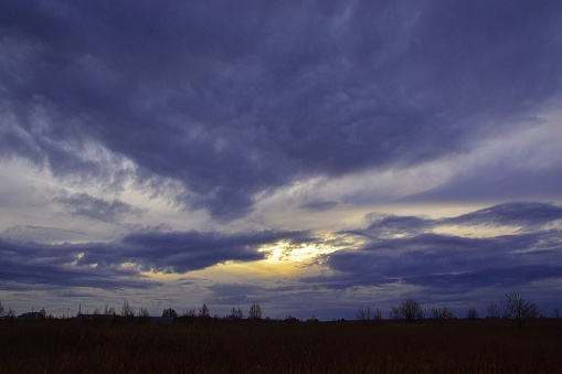 Heavy autumn clouds in the sky at sunset obscure the sun's disk.