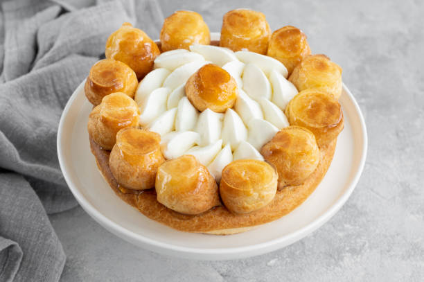 Saint Honore cake with profitrols, caramel, custard and whipped cream on a white plate on a gray concrete background. Traditional French dessert. Copy space. Saint Honore cake with profitrols, caramel, custard and whipped cream on a white plate on a gray concrete background. Traditional French dessert. Copy space choux pastry photos stock pictures, royalty-free photos & images