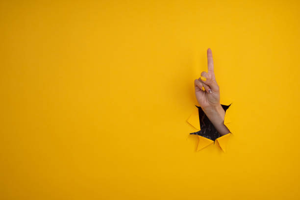 istock Hand point at something out of a hole in torn yellow paper. Left direction, gestures. 1350193818