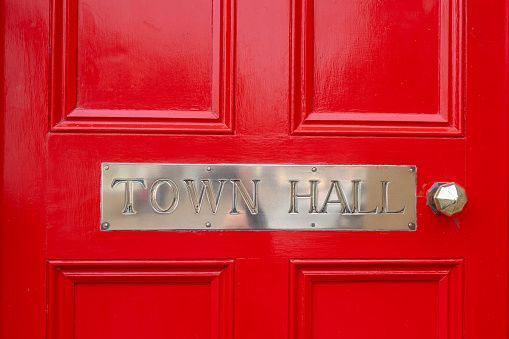 Town Hall silver metal sign. Polished chrome steel sign on bright red wooden door, shiny and clean with stainless steel handle. Capital letters town vintage text.