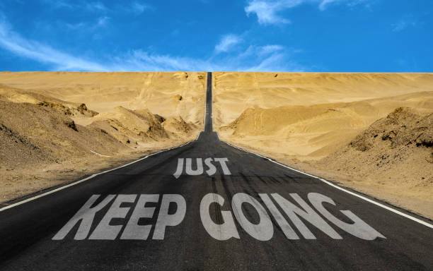 istock Just keep going written on asphalt road. Motivation, quote, team building, self help 1350196288