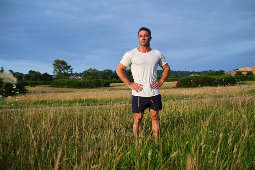 Portrait of a muscular adult man standing on a grassy field with his hands in his waist looking away in the day