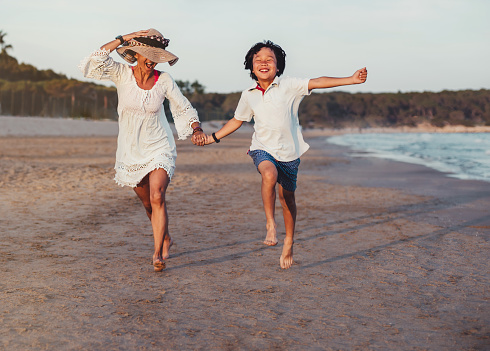 a caucasian mother runs along the beach with her asian son. they are enjoying a day at the beach. concept adoption and vacation. they are happy.
