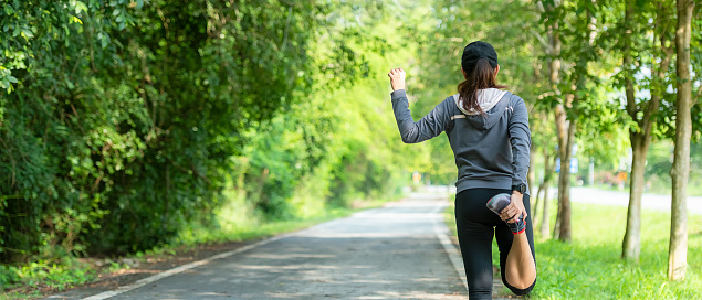 Healthy woman warming up before jogging run and relax stretching her arms and looking away in the road outdoor. Asian runner people workout fitness session, nature park background. copy space for banner