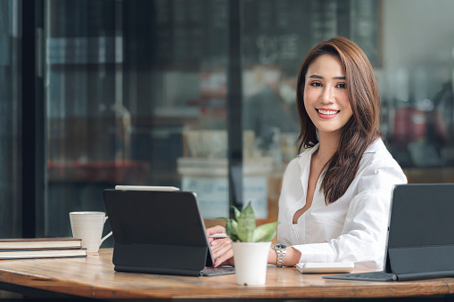 Portrait of young beautiful asian woman smiling and looking at camera while sitting at her office desk, successful business concept,