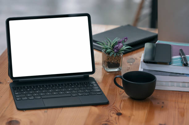 istock Mockup blank white screen tablet with magic keyboard and supplies on wooden table. 1350213706