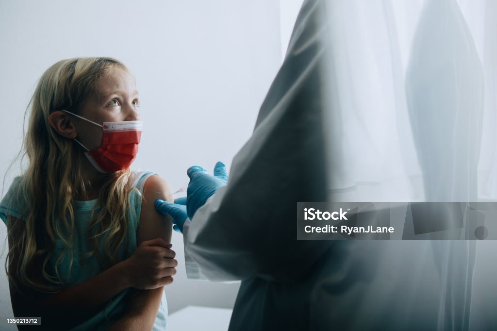 Child Receiving Vaccination Shot From Doctor A Caucasian girl receives a vaccine, possibly for COVID-19 Coronavirus, administered by a female Dr.  She appears fearful and hesitant. Mandate Stock Photo