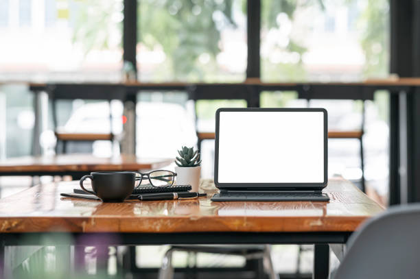 istock Blank screen tablet with magic keyboard and supples on wooden table in cafe room. 1350215022