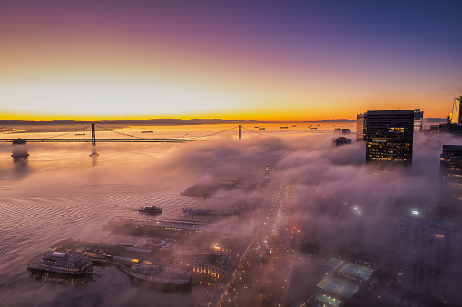 Aerial view of the fog hanging over the Embarcadero in San Francisco as the sun comes up. Skyscrapers and lights below twinkling through the fog.