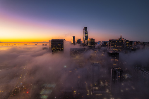 Aerial view of the Financial District in San Francisco from above the fog. Skyscrapers peaking out through the heavy fog and lights twinkling below as the sun comes up.