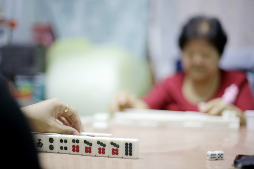 An Asian man is enjoying mahjong game with family members at home - close up on mahjong tile.