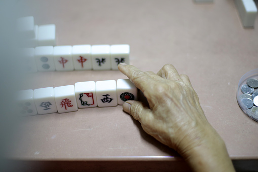 An Asian senior woman is enjoying mahjong game with family members at home.