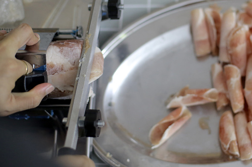 An Asian man is slicing pork using slicer machine at home.