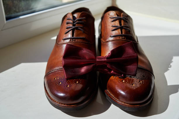 primo piano del papillon da uomo bordeaux su scarpe da uomo in pelle marrone. accessori uomo moderni. dettagli del matrimonio. accessori per lo sposo. outfit casual da uomo con scarpe e papillon - shoe groom wood luxury foto e immagini stock