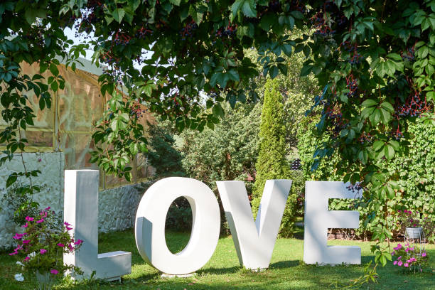 big white letters love on green grass in the garden outdoors, free space. wedding decorations, romantic holiday decor. love sign at wedding reception. valentines day background. love concept - single word love wood typescript imagens e fotografias de stock