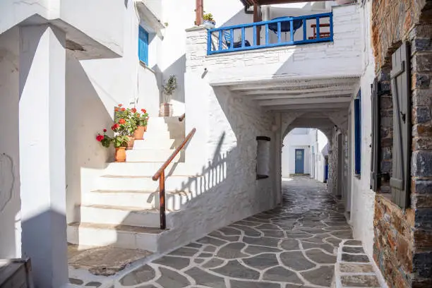 Whitewashed stonewall houses with stairs flowerpots ways covered with shelters cobblestone narrow streets traditional Cyclades architecture. Kythnos island sunny day destination Greece.