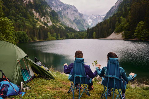 Relaxed couple sitting in camping chairs outside tent while camping by the lake