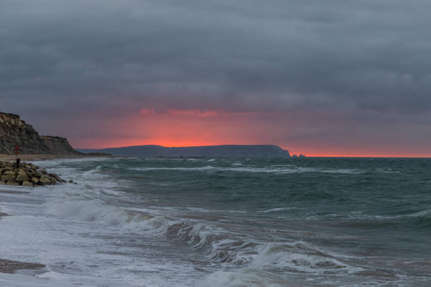 A scenic and dramatic sunset over a choppy sea with dark black thundery sky
