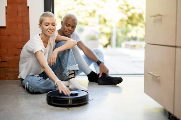 istock Couple sitting on floor with robot vacuum cleaner 1350248515