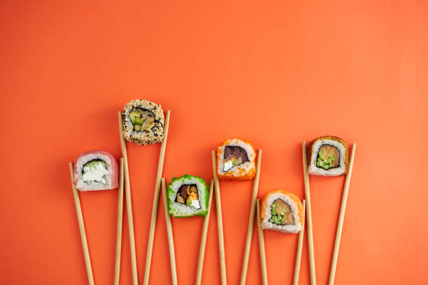Different types of sushi rolls with tuna, eel, salmon. Mockup with chopsticki and sushi on orange background