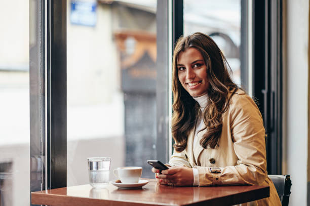 istock Woman using a smartphone and drinking coffee while sitting in a coffee shop 1350249511