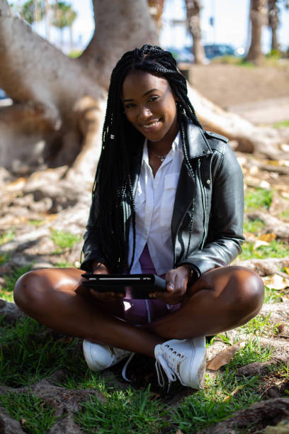 istock beautiful african female student smiling sitting in a park 1350253596