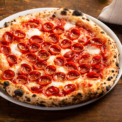 Freshly baked Neapolitan pizza with pepperoni and mozzarella cheese on a wooden table