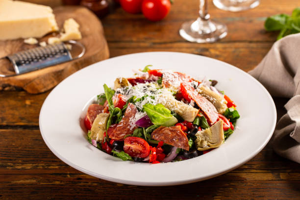 italienischer antipasti-salat mit salami, artischockenherzen und oliven - antipasto stock-fotos und bilder