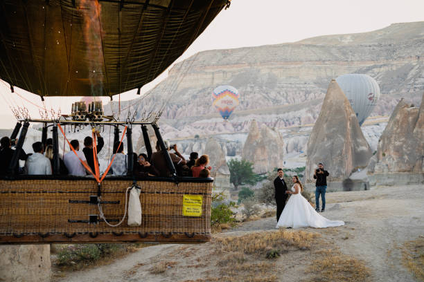 hot air balloon basket with tourist flying near a wedding couple Goreme, Turkey - August 3, 2021: Close up of hot air balloon with basket full of tourist flying very close and spurring a wedding couple celebrating on the ground in Cappadocia unusual basket stock pictures, royalty-free photos & images