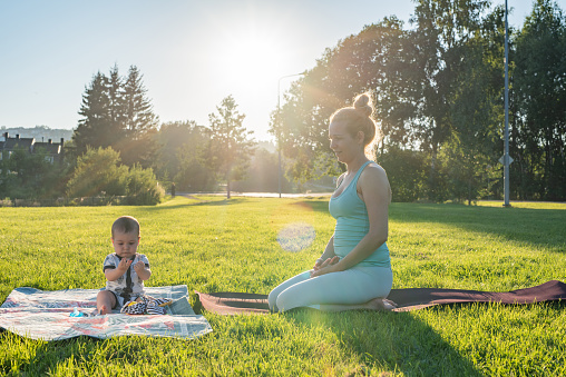Mother and her little son sitting on the blanket in public park during summer day