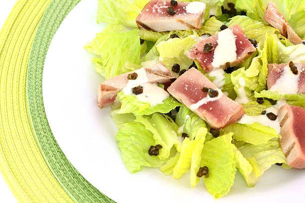 Caesar Salad A photograph of a plate of Grilled Tuna Caesar Salad made with romaine lettuce, sliced grilled tuna steak, fried capers drizzled with Caesar dressing. caesar salad food salad tuna stock pictures, royalty-free photos & images