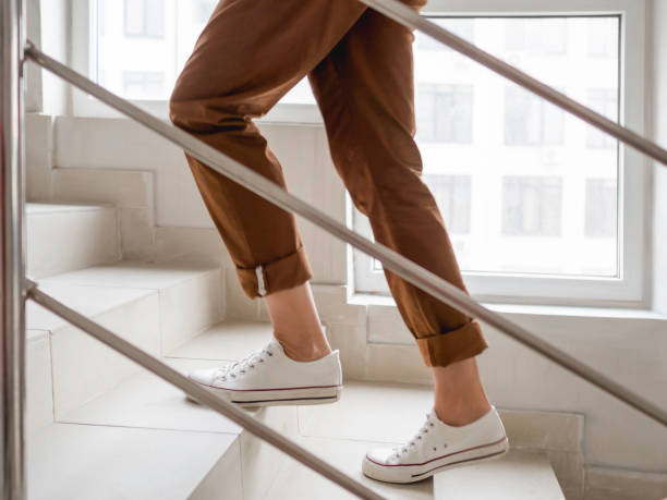 mujer con zapatillas blancas y pantalones caqui sube las escaleras a su apartamento. escalera blanca en edificio de apartamentos. outfit casual, moda urbana. - staircase fotografías e imágenes de stock