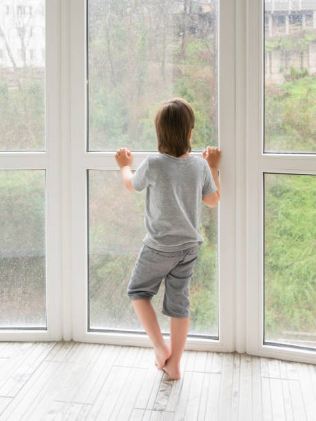 istock Little boy looks outdoors through wet panoramic window with raindrops. Coronavirus COVID19 quarantine. Rainy summer weather. Kid stays alone at home. Loneliness and sad mood without children's company. 1350290551