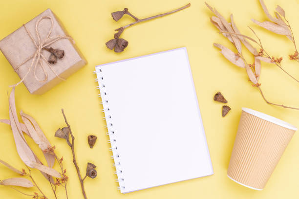 istock Autumn composition. Blank notebook with a spring, a gift wrapped in kraft paper, autumn leaves, paper eco glass on a yellow background. Flat lay, top view, copy space 1350291865