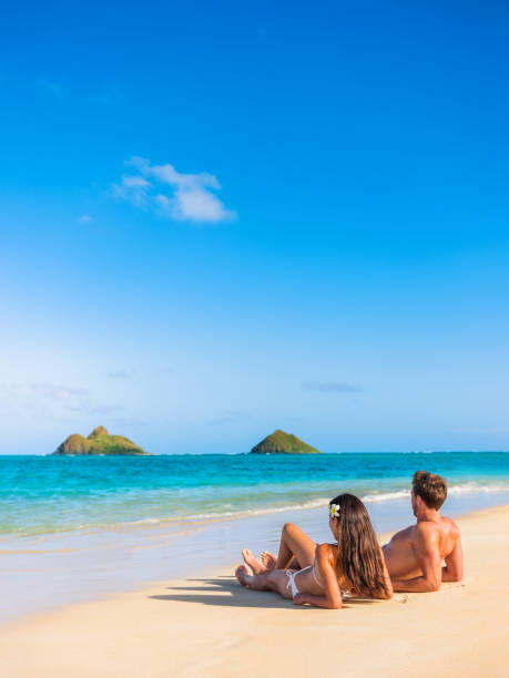 pareja de vacaciones en la playa tomando el sol en la playa tropical hawaiana en lanikai, oahu, hawái, ee. uu. los estadounidenses en vacaciones de verano bronceándose al sol acostados en la arena - hawaii islands fotos fotografías e imágenes de stock