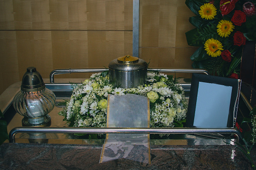 Memorial service before burial with visible picture frame, metal urn with ashes and bouquet. Sad grieving moment.