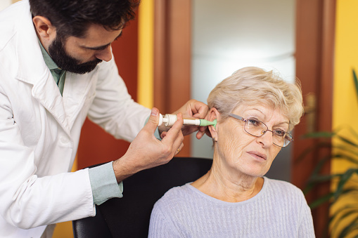 Doctor audiologist using syringe and injecting special foam to get shape if ear inside and to get perfect hearing aid for his senior adult patient in doctor's office