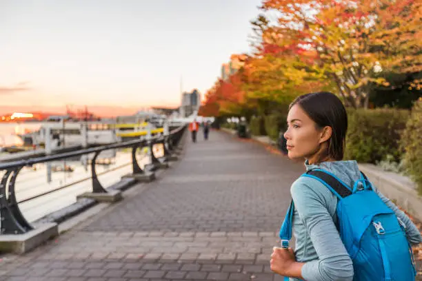 Photo of Vancouver city urban lifestyle people at Harbour, British Columbia. Woman tourist with student backpack in city outdoors enjoying autumn season