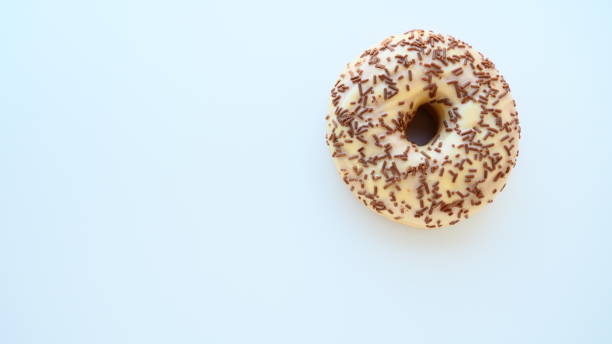 istock Doughnut close-up on white or gray background. Delicious cake covered with vanilla icing and chocolate sprinkles. High-calorie breakfast or snack. Sweet dessert with vanilla and chocolate, donut or dough. 1350320142