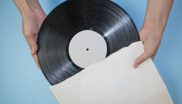 istock Hands hold an old vinyl record in an old paper case on a light blue background. 1350320706