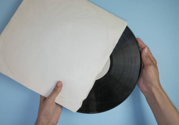 istock Hands hold an old vinyl record in an old paper case on a light blue background. 1350320707
