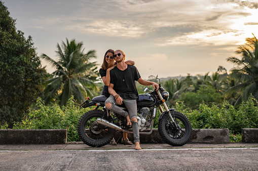 Smiling couple is sitting  on the motorcycle and looking at camera at sunset.