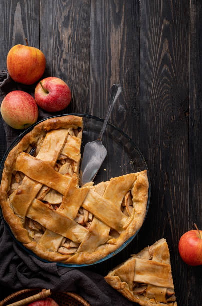 Top view of homemade apple pie on black wooden table Autumn foods. Top view of homemade apple pie on dark wooden table, decorated with apples, sugar and tablecloth apple pie stock pictures, royalty-free photos & images