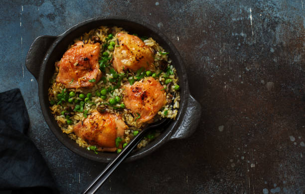 Fried chicken thighs with orzo pasta and green peas in a skillet on dark stone background stock photo