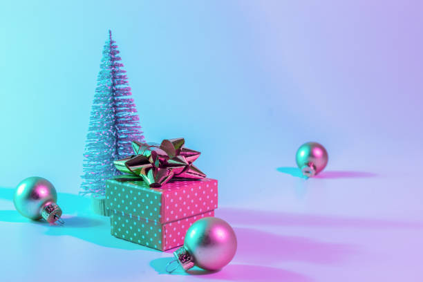 istock Neon xmas winter background. Holiday decoration bauble ball on neon gradient backdrop. Minimal abstract tree, xmas gift box. Happy new year copy space. 1350364060