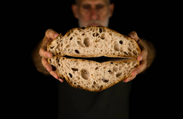 istock Adult man holding bread cut in half against black background 1350366775