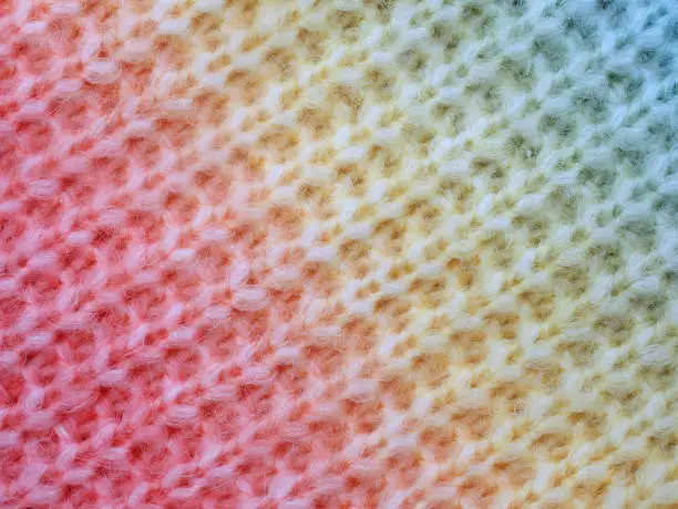 knitted cotton structure with a gradient from red to yellow to blue, close up of knitted cotton surface.