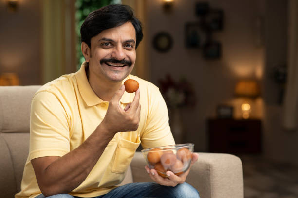 man eating sweet food, stock photo Indian, Indian ethnicity, lifestyle, adult, eating, sweet food, Gulabjamun, domestic room, india sweets stock pictures, royalty-free photos & images